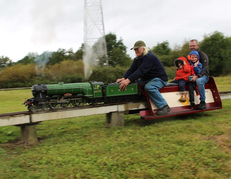 large green steam locomotive with driver and three passengers